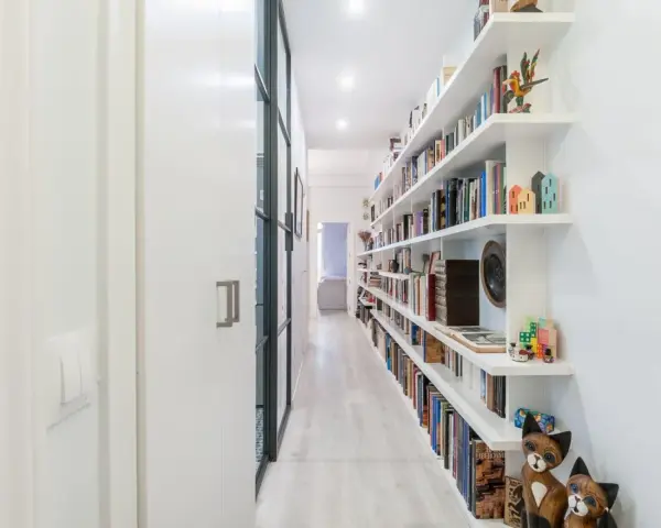 Pasillos estrechos y modernos con estanterías blancas repletas de libros y objetos decorativos, creando un ambiente acogedor.