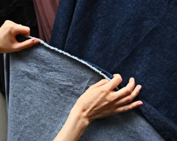 Dłonie dotykają ciemnoniebieskiego denimu i szarej tkaniny, być może z domieszką elastanu, sprawdzając ich fakturę.