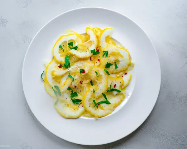 Dünne Scheiben Zitrone mit Zucker bestreut, garniert mit frischen Kräutern und Chiliflocken. Ein erfrischender Genuss!