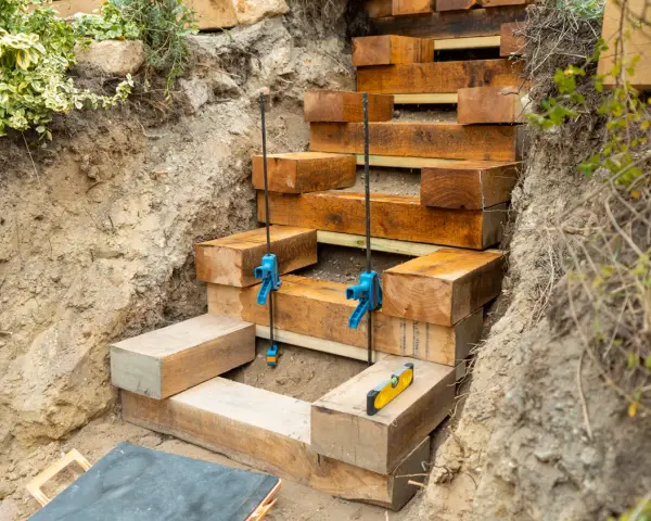 Construction d'un escalier traverse bois et gravier. Des poutres de bois sont empilées pour former des marches dans une tranchée.
