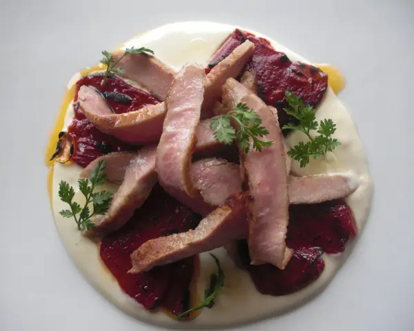 Lonchas de cerdo tierno sobre una cama de puré cremoso y pimiento del piquillo asado, decorado con perejil fresco.