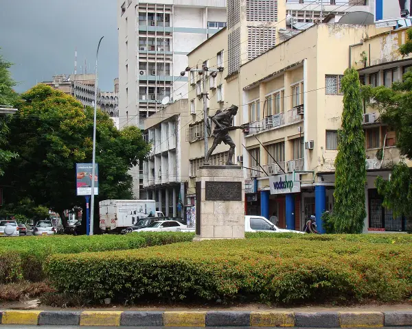 Pomnik żołnierza na tle budynków w Dar es Salaam. W tle widać ruch uliczny i drzewa.