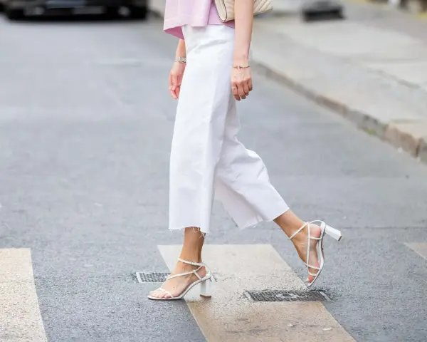 Mujer cruza la calle con un look comunión: pantalón blanco de corte ancho y sandalias de tiras.