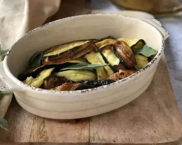 Zucchine in carpione dorate e saporite, guarnite con foglie di salvia fresca, servite in una ciotola rustica.