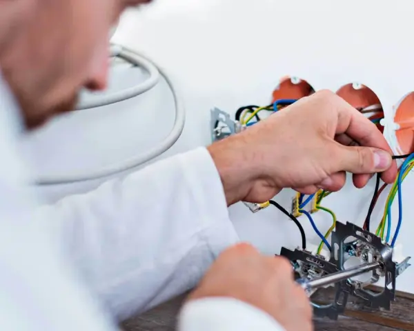 Elektryk dokonuje wymiany instalacji elektrycznej, podłączając przewody do puszek.