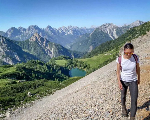 Una donna fa una camminata outdoor in montagna, godendosi il panorama di un lago alpino e vette maestose. Il vero significato di camminata outdoor è qui.