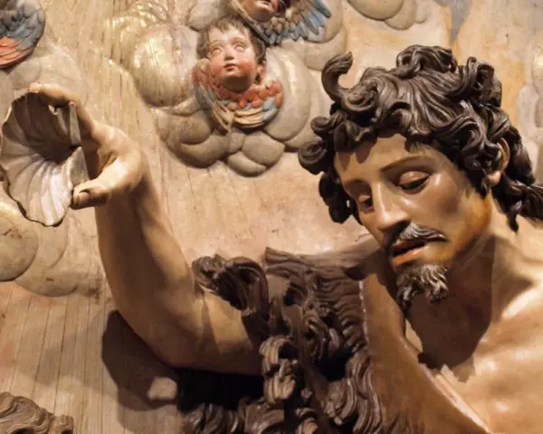 Detalle de escultura barroca: figura masculina con barba y cabello rizado sostiene una concha. Ángeles infantiles observan. Maestría de escultores del barroco.