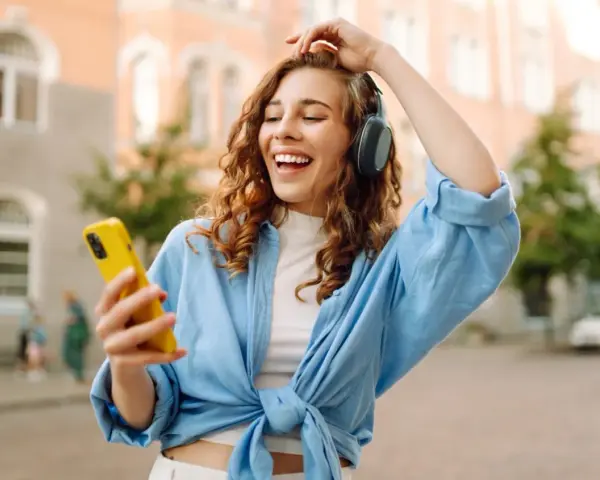 Kobieta w słuchawkach i niebieskiej koszuli trzyma żółty telefon, słuchając muzyki.
