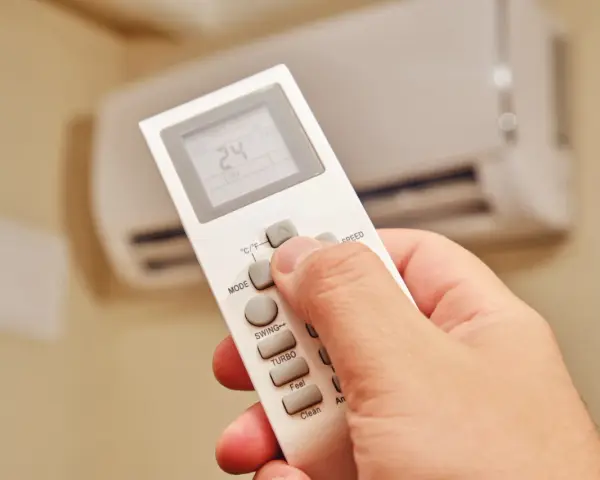 Dłoń trzymająca pilot do klimatyzatora, ustawiająca temperaturę 24°C. Ogrzewanie klimatyzatorem zapewnia komfort.