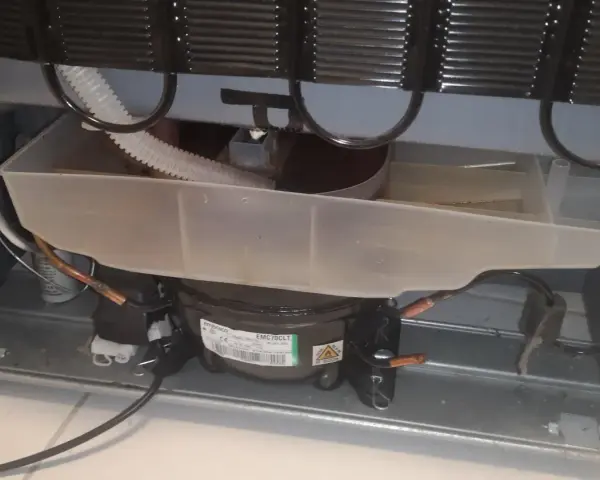 Widok wnętrza lodówki Whirlpool z widocznym kompresorem i tacą skraplacza.