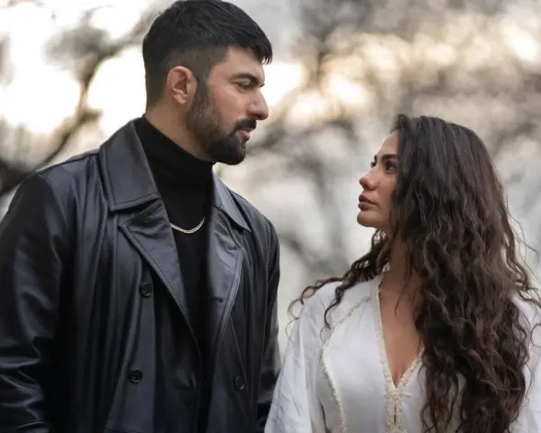Un uomo con trench di pelle nera e una donna con lunghi capelli scuri si guardano intensamente. Io sono Farah, e questo sguardo dice tutto.