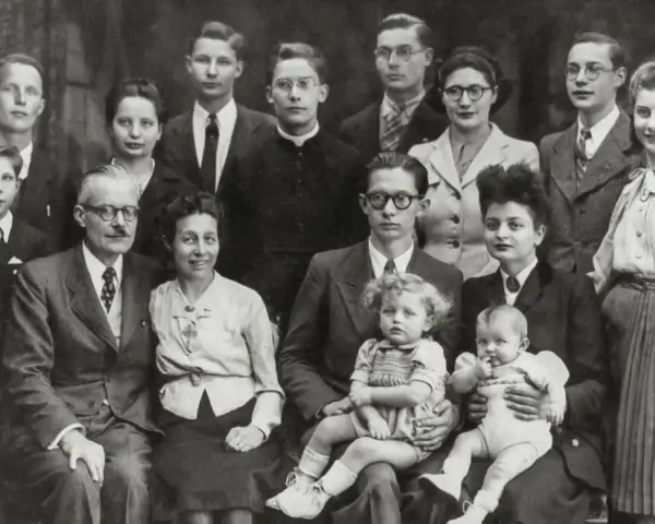 Gros plan sur une famille nombreuse posant pour une photo. On peut y voir des enfants, des adultes et des bébés. Une recherche sur Geneanet pourrait révéler leur nom de famille.