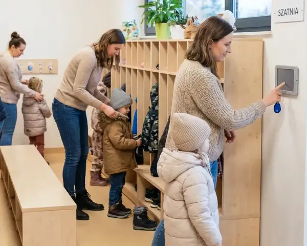 Rodzice z dziećmi w szatni, przygotowujący się do wyjścia. System kontroli zarządczej ułatwia zarządzanie wejściami i wyjściami.