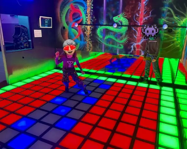 Kinder spielen im **underground lasergame Berlin** auf einer leuchtenden Tanzfläche. Bunte Drachen zieren die Wand.