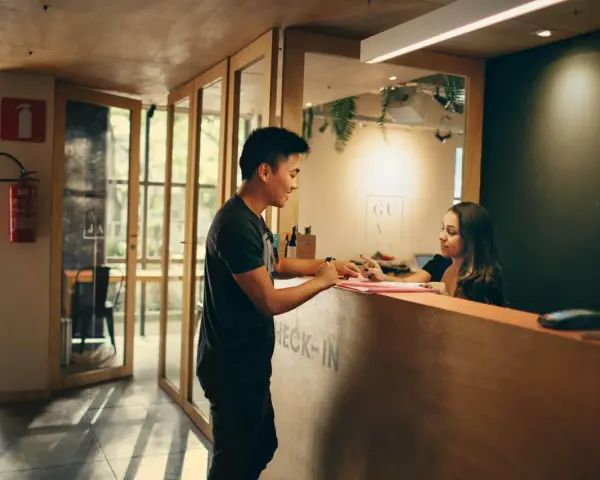 Mężczyzna melduje się w hotelu. Pracownica recepcji wyjaśnia, ile zarabiają turcy w hotelach, gdy obsługuje gościa.