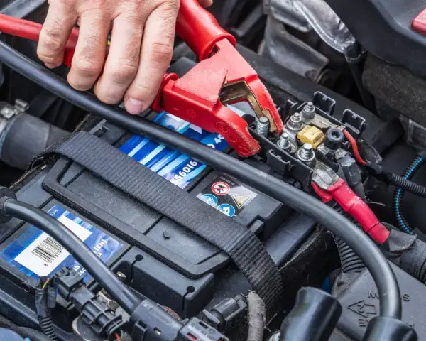 Starthilfe war zuerst: Eine Hand befestigt eine rote Klemme an der Autobatterie, um dem Fahrzeug wieder Leben einzuhauchen.