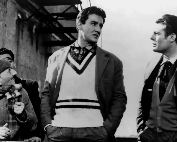 Uomini in abiti d'epoca, uno con un maglione a V, discutono animatamente. Un'iconica scena della commedia all'italiana.
