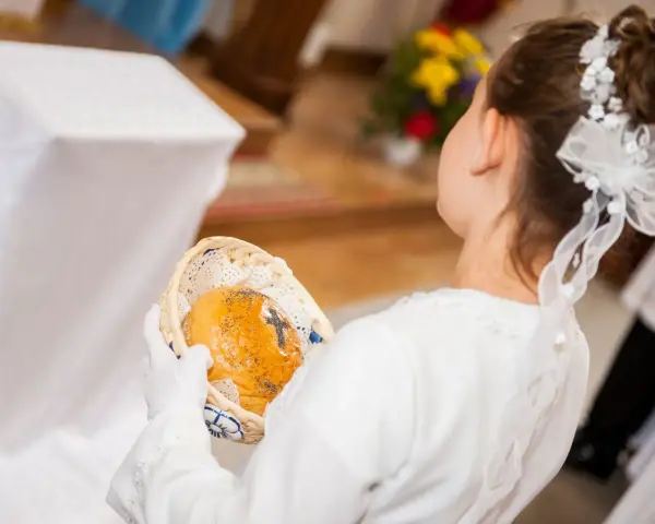 Dziewczynka w bieli trzyma koszyczek z opłatkiem. Zastanawiasz się, ile daje chrzestny na komunię?