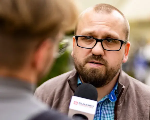 Mężczyzna w okularach udziela wywiadu mikrofonowi radiowemu.
