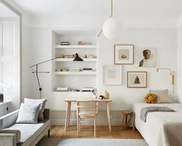 Accogliente camera da letto minimal con letto singolo, scrivania in legno, divanetto e quadri alle pareti.