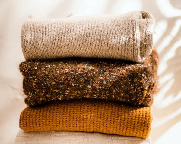 Gestapelte Strickwaren in warmen Herbstfarben. Damit die **Wolle bei 40 Grad waschen** gelingt, sind diese Pullover perfekt.