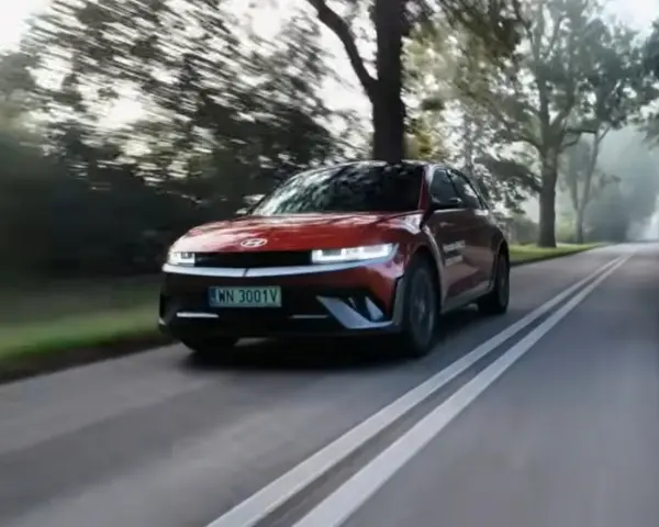 Czerwony Hyundai Ioniq 5 jedzie po wiejskiej drodze wśród drzew.