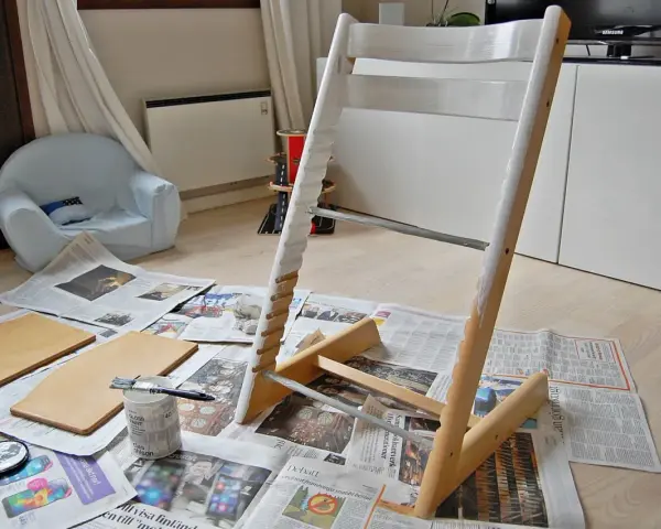Måla om Stokke stol med vit färg. Trädelar och pensel ligger på tidningspapper.