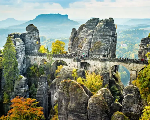 Most Bastei, skalne miasto w Saksonii, z kamiennym mostem łączącym skalne iglice. Jesienne liście dodają koloru krajobrazowi.