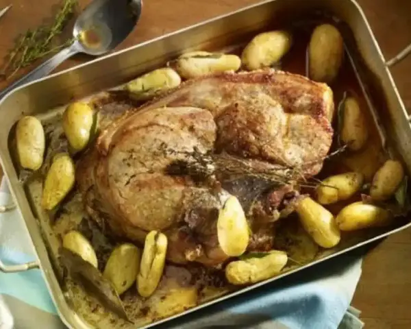 Rouelle de porc rôtie au four, entourée de pommes de terre dorées et d'herbes aromatiques. Un plat savoureux prêt à être dégusté.