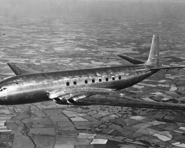 Pierwszy samolot pasażerski, lśniący de Havilland Comet, przelatuje nad patchworkiem pól.