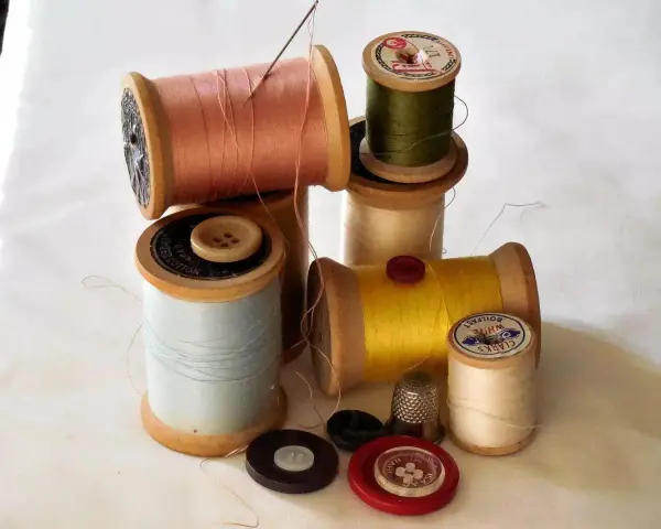 Bobine di filo colorato, bottoni e un ditale, pronti per un punto sopraggitto a mano.