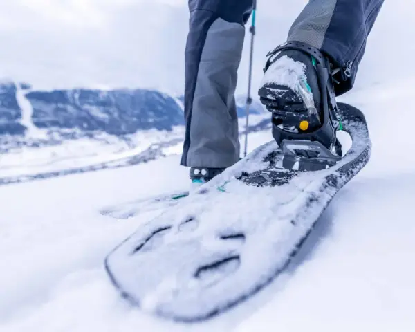 Piede con racchette da neve che affonda nella neve fresca, pronto per camminare in montagna.