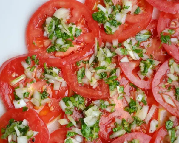 Fette di pomodoro fresco condite con cipolla tritata e erbe aromatiche. Un'insalata di pomodori semplice e gustosa.