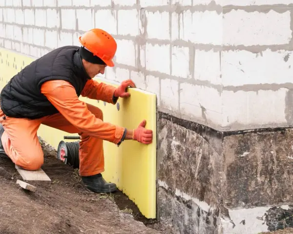 Budowlaniec układa izolację na nierównych fundamentach. Jak zaizolować stare nierówne fundamenty? To klucz do ochrony domu.