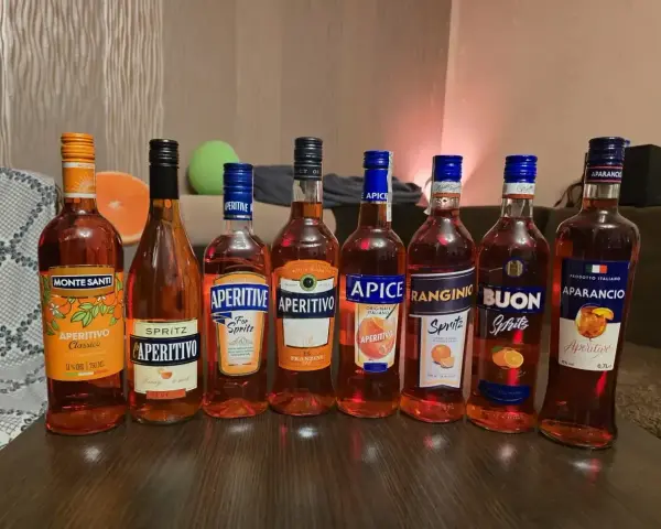 Rząd pomarańczowych butelek aperitifów, w tym Campari i Aperol, gotowych na wieczór.