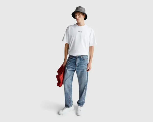 Uomo con t-shirt bianca "LOVE", cappello bucket grigio e jeans relaxed fit. Il significato di questi jeans è comfort e stile casual.
