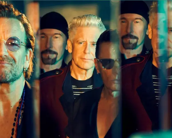 Le groupe U2, avec Bono au premier plan, pose en groupe, leurs visages reflétant une lumière tamisée.