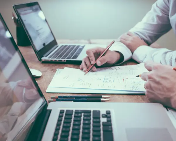 Deux personnes travaillent sur des documents et des ordinateurs portables, discutant du droit de la mode.