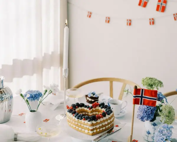 Festligt dukat bord med hjärtformad tårta, blommor och norska flaggor. Perfekt för firande med flaggor att skriva ut.