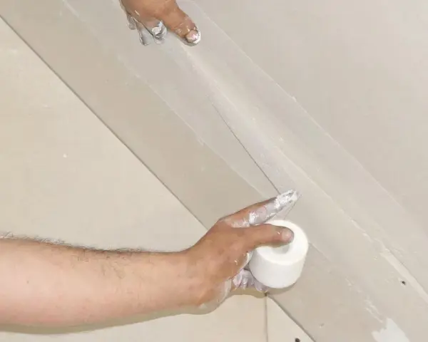 Hände arbeiten an einer q4 Spachtelung. Eine Rolle Klebeband wird gehalten, während die andere Hand die Spachtelmasse aufträgt.