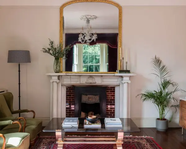 Sofá verde, chimenea con espejo dorado y candelabros. La sala de estar exhibe colores elegantes y un ambiente acogedor.