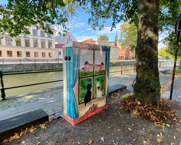 En målad låda med två katter som tittar ut genom ett fönster på ett slott. Konstnären har valt att måla tunt för att ge en drömsk känsla.