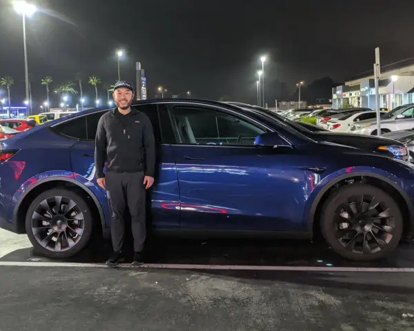 Mężczyzna stoi obok ciemnoniebieskiego Tesli Model Y na nocnym parkingu.