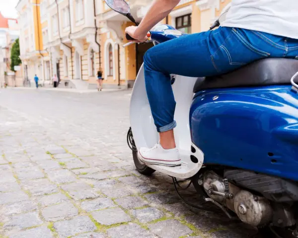 Un uomo in jeans guida uno scooter blu su un lastricato, un'immagine che evoca la libertà e lo spirito dell'art 52 cds.