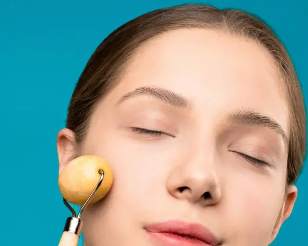 Mujer con ojos cerrados disfrutando de un masaje facial antienvejecimiento y drenaje con rodillo de jade.