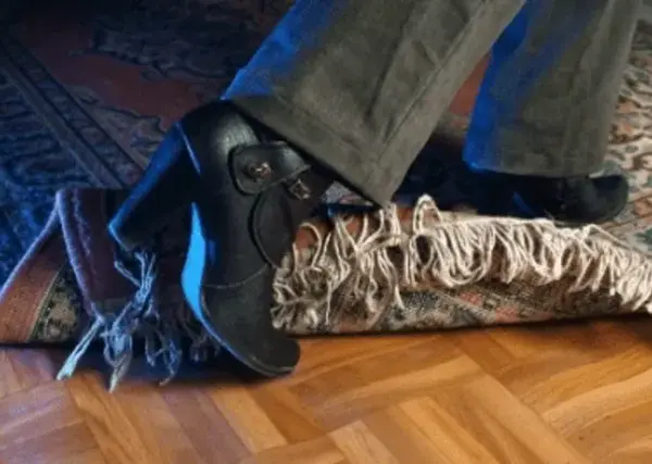 En fot med klacksko snubblar på en matta. En antiglidmatta hade kunnat förhindra detta.