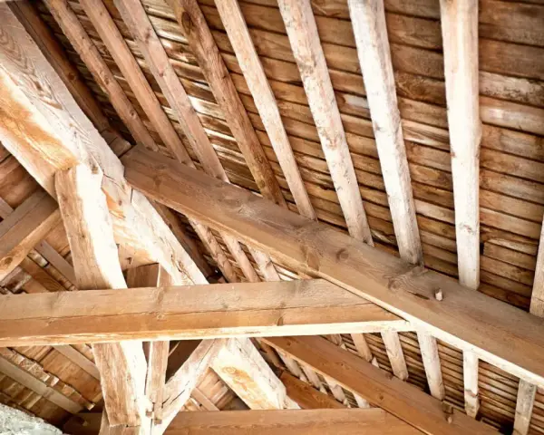 Vue rapprochée d'une charpente ancienne en bois, témoignant d'un savoir-faire artisanal. Un futur projet de traiter charpente pour la préserver.