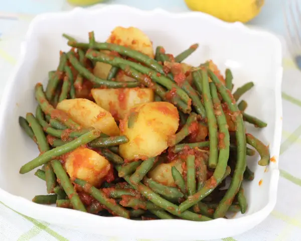 Fagiolini in umido con patate, un piatto saporito e colorato, servito in una ciotola bianca su una tovaglia a quadri.