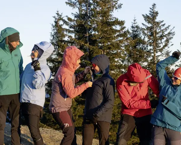Sechs Personen in bunten Hardshelljacken stehen vor Bäumen. Eine Hardshelljacke schützt vor Wind und Wetter.