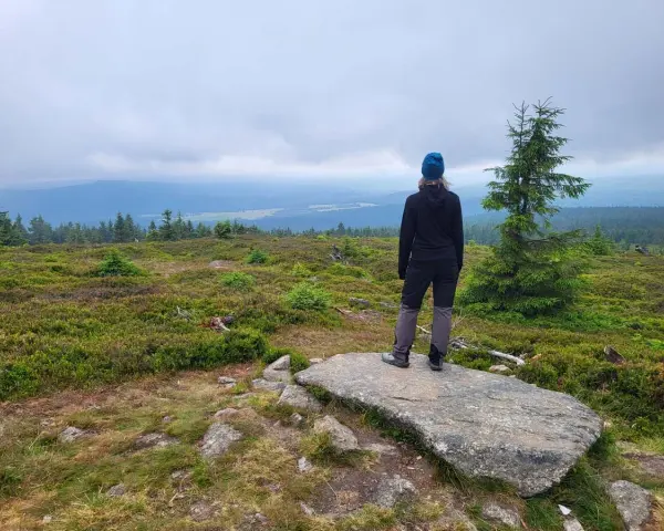 Widok z najwyższego szczytu Gór Izerskich. Kobieta w czapce i kurtce podziwia rozległą panoramę.